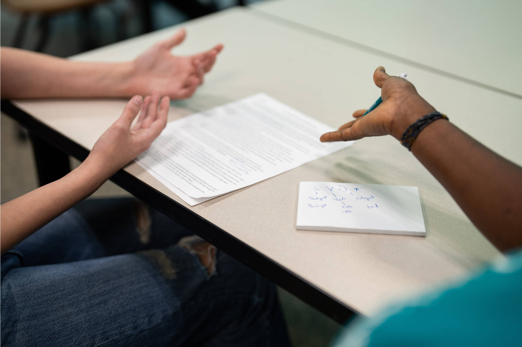 A zoomed in look of a student's hands and consultant's hands referencing a paper